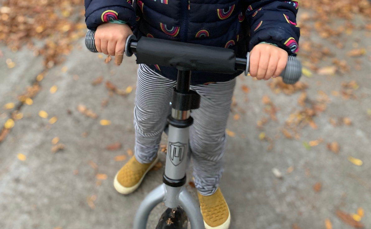 Grey MambaBikes Balanced Bike with a child wearing yellow shows and stripes pants